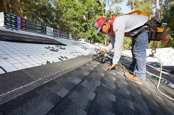 Roofer nailing new architectural shingles during replacement